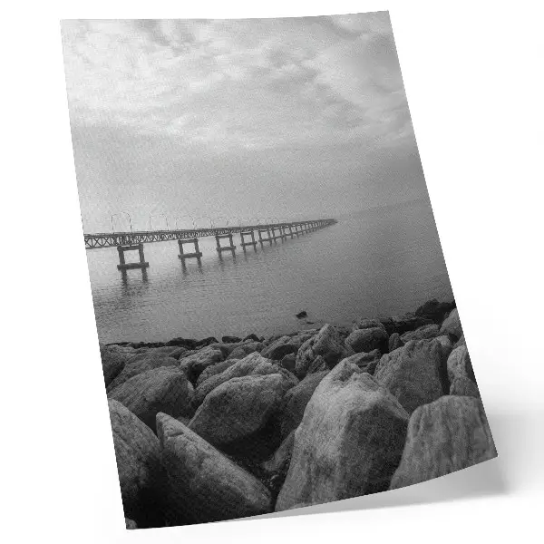 Hållbar väggposter fridfullt landskap med bro och stenig strand under en grå himmel