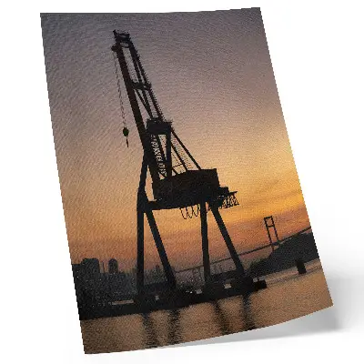 Hållbar väggposter industriell kran i silhuett mot en bro i solnedgång