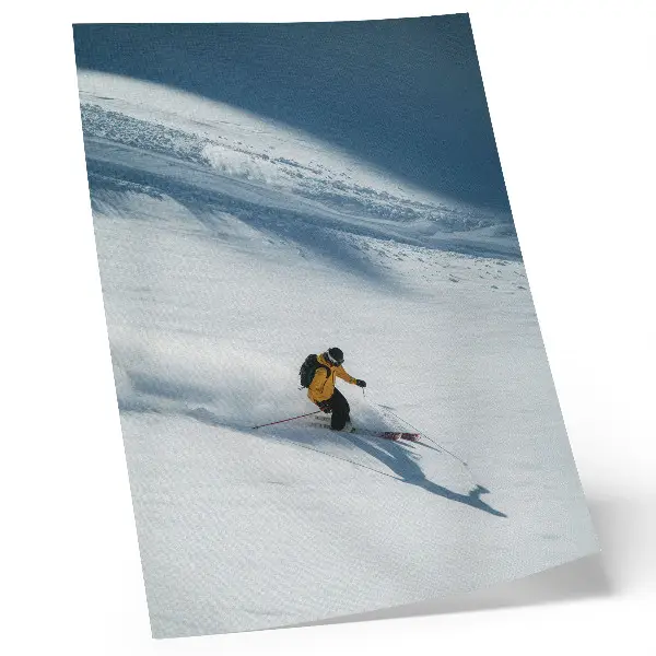 Poster skidåkare i gul jacka i en snöig sluttning med skugga