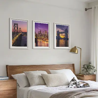 Tavelset ovanför soffa med motiv av broar, sol och stadsutsikt