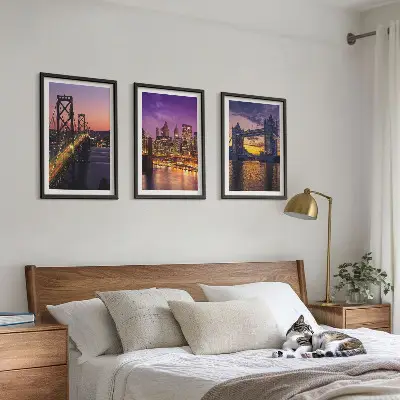 Tavelset ovanför soffa med motiv av broar, sol och stadsutsikt