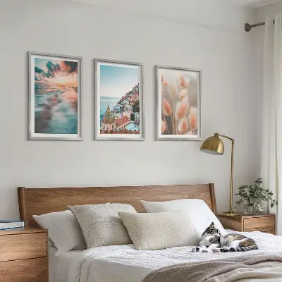Tavelset ovanför soffa med motiv av hav, solnedgång, hus och blommor