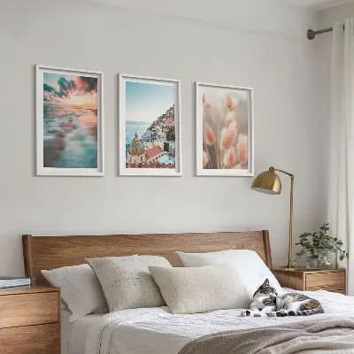 Tavelset ovanför soffa med motiv av hav, solnedgång, hus och blommor
