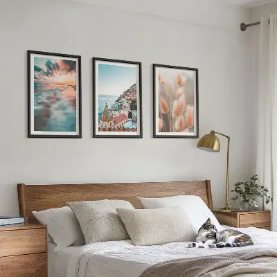 Tavelset ovanför soffa med motiv av hav, solnedgång, hus och blommor
