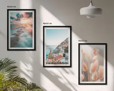 Tavelset ovanför soffa med motiv av hav, solnedgång, hus och blommor