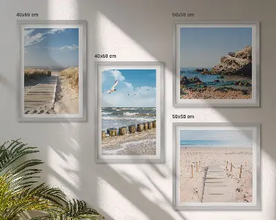 Tavelvägg ovanför soffa med motiv av strand, sand, vågor, himmel och fåglar