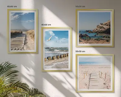 Tavelvägg ovanför soffa med motiv av strand, sand, vågor, himmel och fåglar
