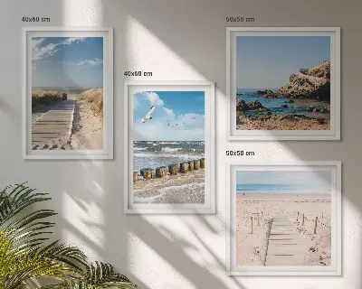 Tavelvägg ovanför soffa med motiv av strand, sand, vågor, himmel och fåglar