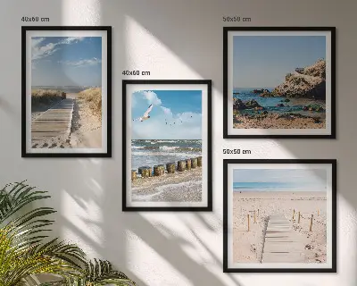 Tavelvägg ovanför soffa med motiv av strand, sand, vågor, himmel och fåglar