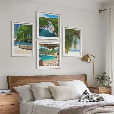 Tavelvägg ovanför soffa med motiv av strand, båt, vattenfall och palmer