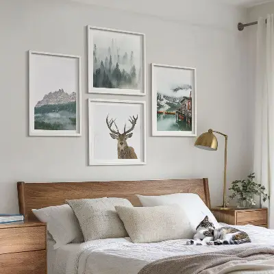 Tavelvägg med motiv av berg, sjö, rådjur, hydda och dimma ovanför soffan
