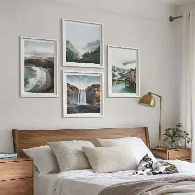 Tavelvägg ovanför soffa med motiv av berg, stränder, moln och vatten