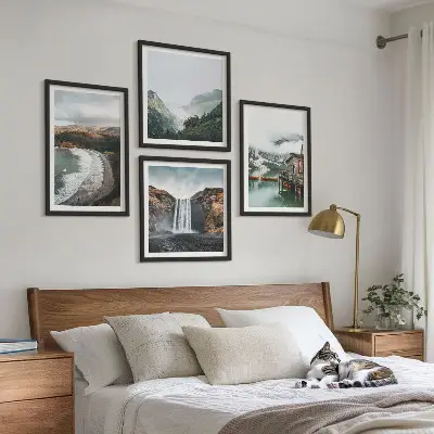 Tavelvägg ovanför soffa med motiv av berg, stränder, moln och vatten